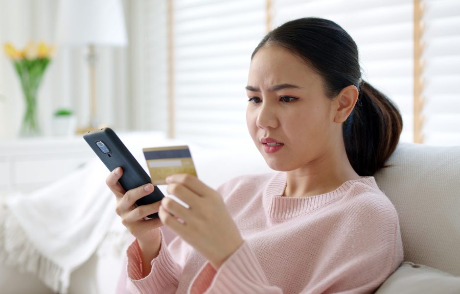 woman with confused look holding phone and credit card