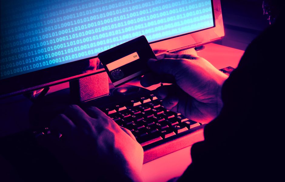 hacker on a computer in the dark looking at the back of a stolen credit card